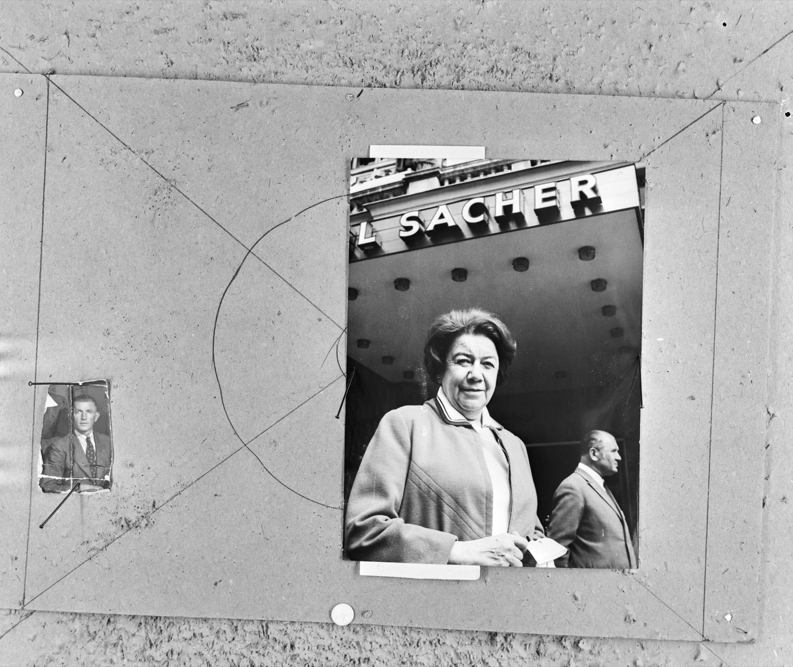 Black-and-white press-agency contact scan: an older woman in a light coat with a dark collar, hair pulled back, standing and facing the camera below an illuminated 'Sacher' hotel sign in Vienna, with a smaller unrelated portrait of a young man taped at the left edge.