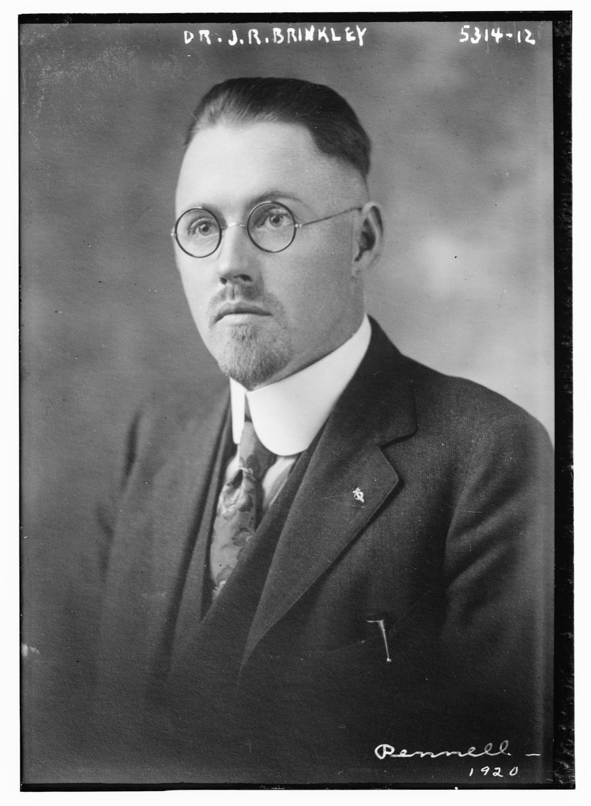 Black-and-white studio portrait of a bespectacled man in a suit, captioned Dr. J.R. Brinkley.
