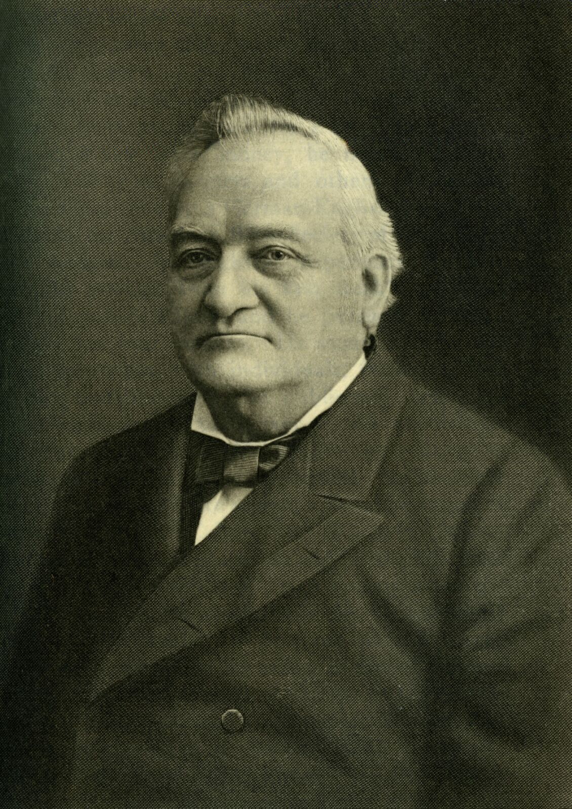 A formal studio portrait of an elderly man with white hair combed back, a heavy mustache-free jaw, wearing a dark suit, wing collar, and bow tie, looking slightly off-camera.