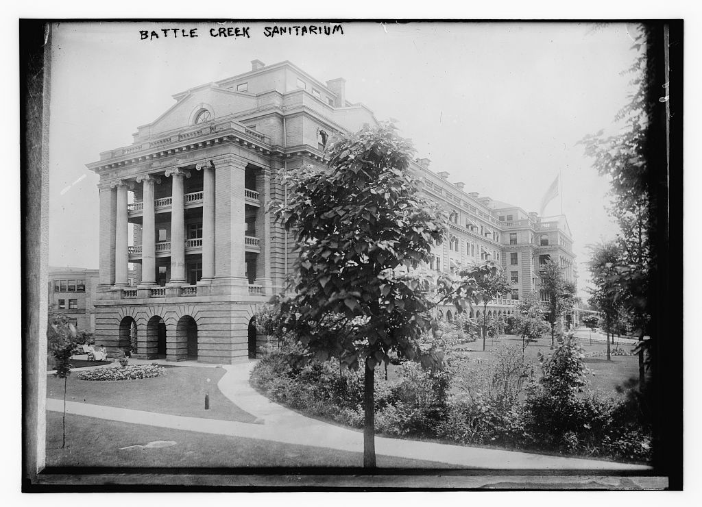 Black-and-white photograph of a large multi-wing institutional building with a colonnaded portico, lawn and trees in the foreground.