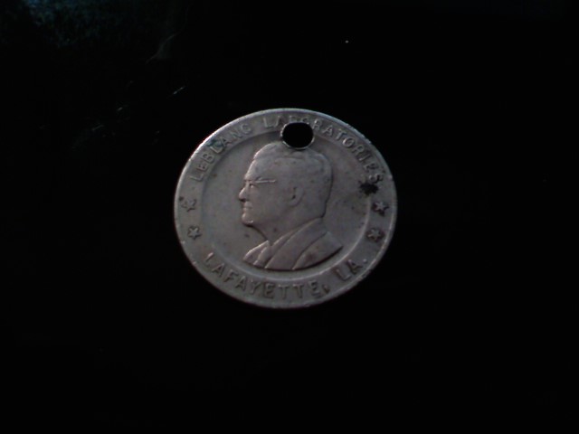 The front face of a worn metal trade token, showing a raised profile bust of a bespectacled man encircled by the text 'LEBLANC LABORATORIES' and 'LAFAYETTE, LA'.