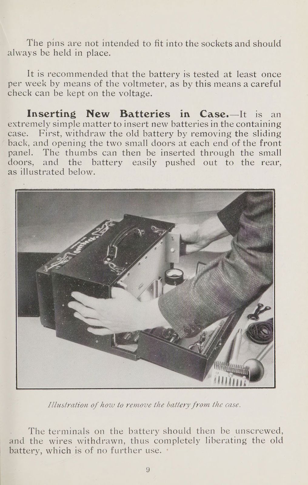 Black-and-white photograph of a metal boxed apparatus on a table, its sliding back open and a hand reaching inside; rod and comb electrodes and cords lie beside it.