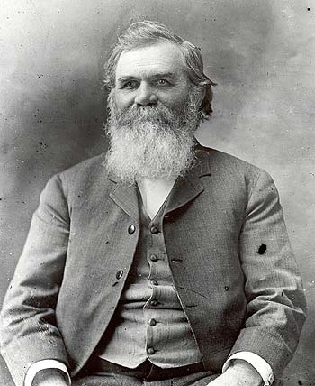 Black-and-white studio portrait of an older bearded man in a formal three-piece suit, facing slightly to the side.