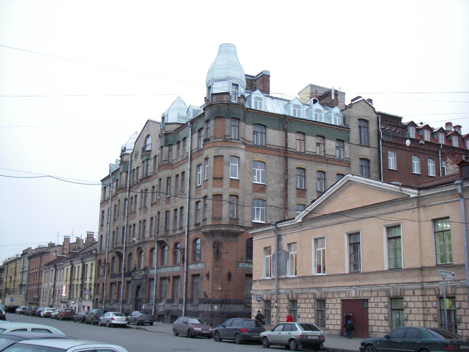 A 19th-century corner apartment building in Saint Petersburg with a rounded brick turret topped by a glazed cupola, seen from the street with parked cars; a modern colour photograph